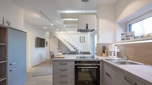 A modern kitchen with a built-in oven, a dining area with a table and chairs, and a staircase leading to another level. - Ferienwohnung in Husum (Husum)