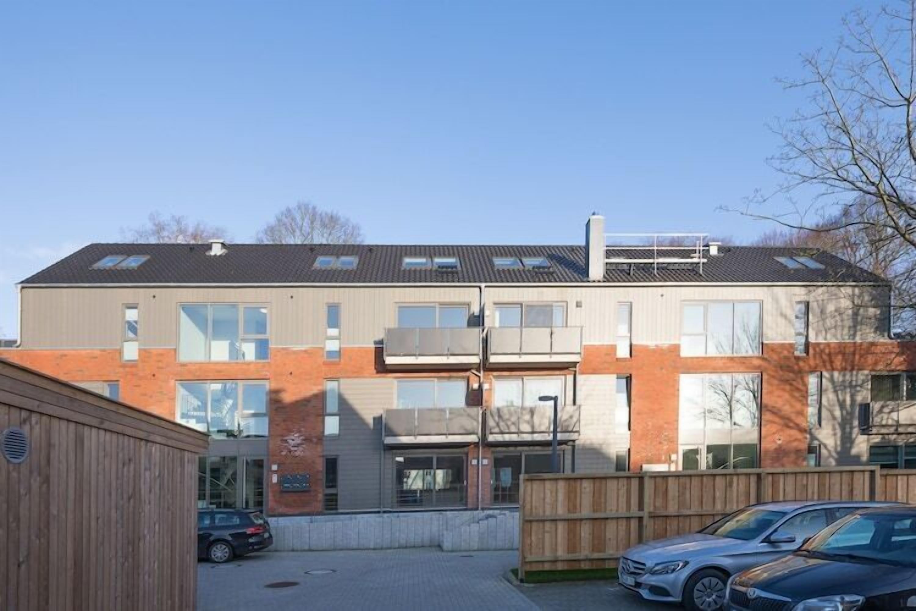 Un edificio moderno de varios pisos con amplios ventanales, techo plano y valla de madera al frente.