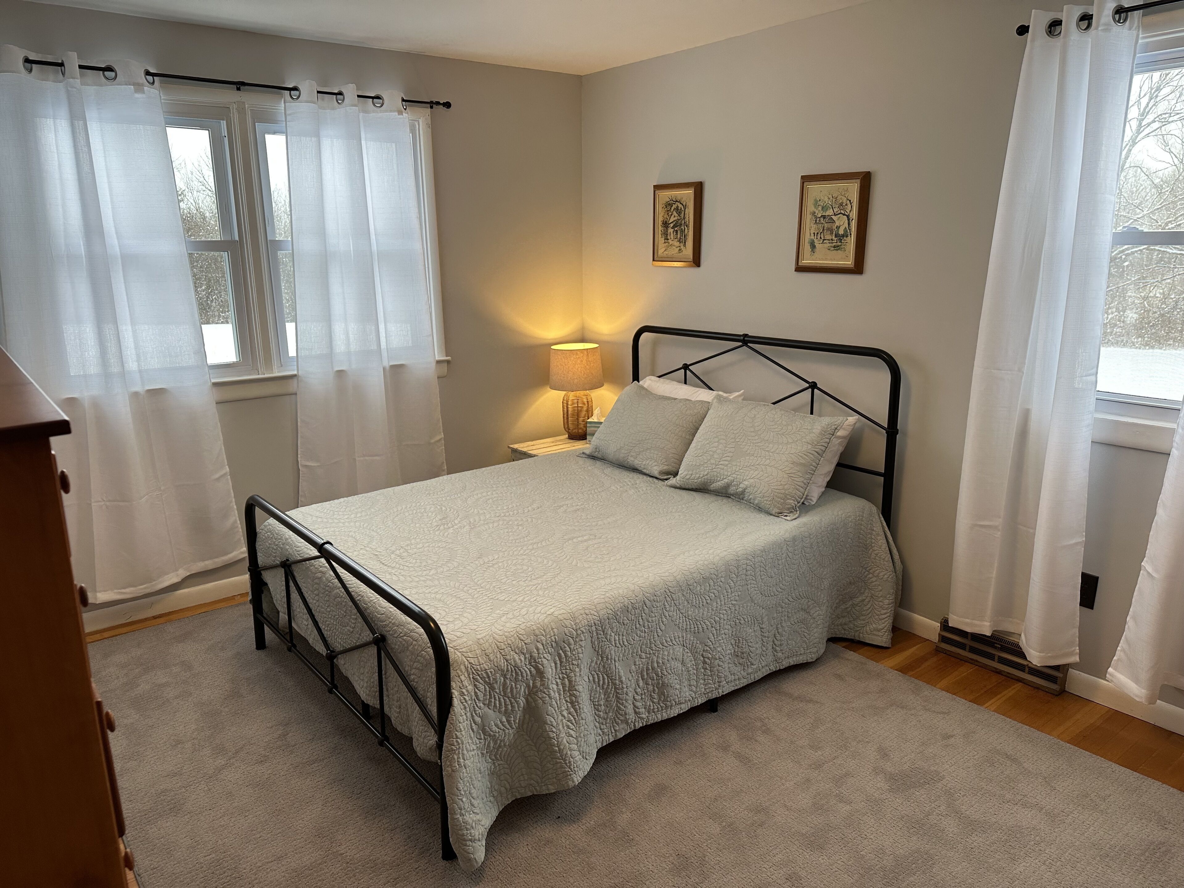 A neatly arranged bedroom with a bed, a bedside lamp, and two framed pictures on the wall.