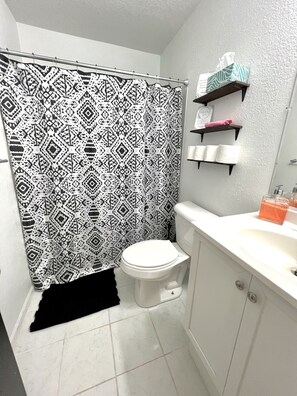 A bathroom with a patterned shower curtain, a toilet, a sink with toiletries, and a towel rack.