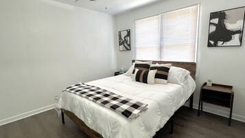 Un dormitorio con una cama, una mesita de noche, un ventilador de techo y dos obras de arte colgadas en la pared.