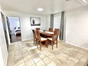 A dining area with a wooden table and chairs, a framed picture on the wall, and a view into another room.