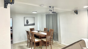 Un coin repas avec une table et des chaises en bois, un projecteur fixé au plafond et un tableau encadré au mur.