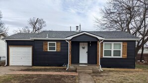 Une maison à deux étages, à l’extérieur sombre, avec un garage et une véranda à l’avant.