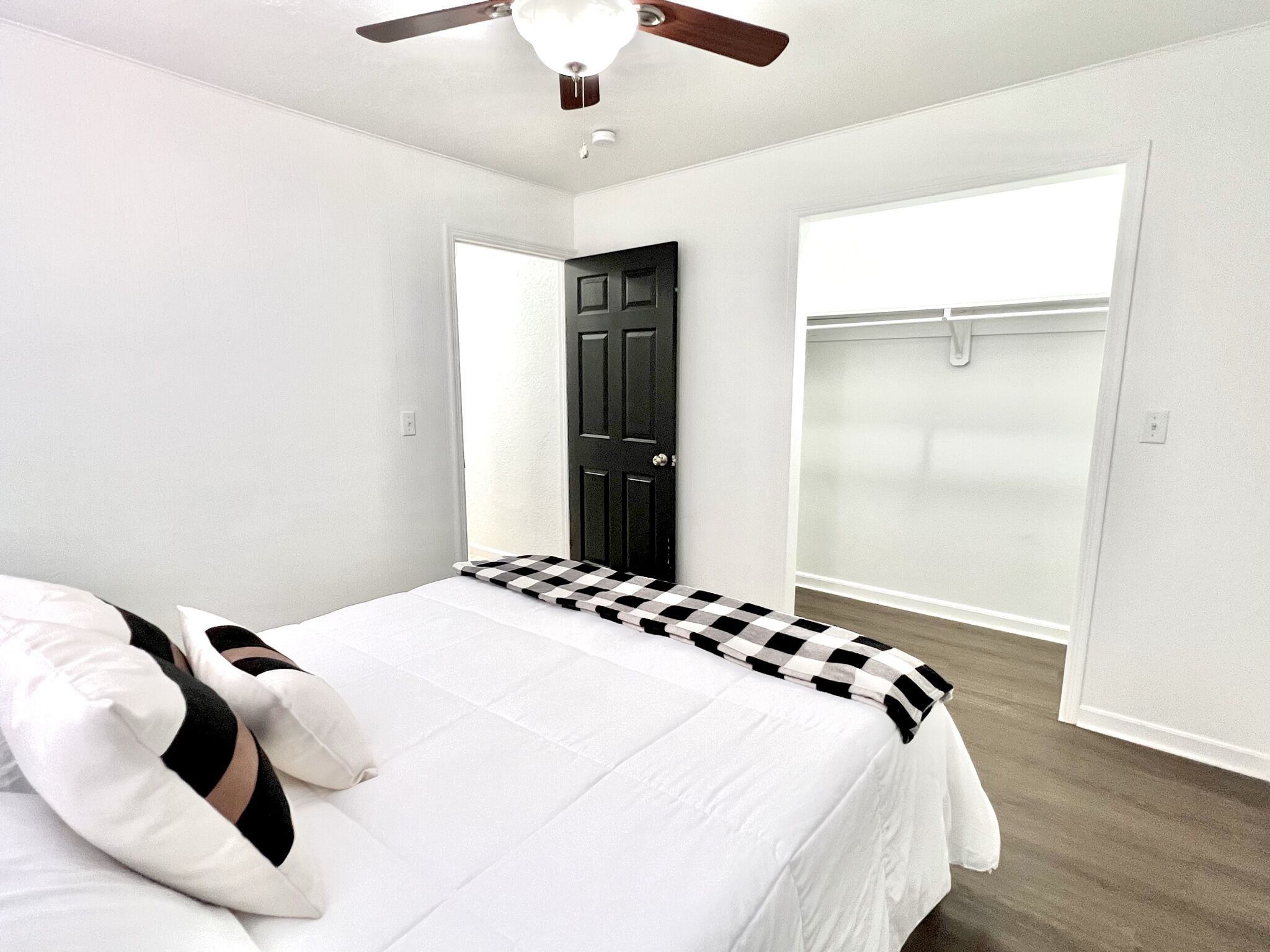 Un dormitorio con una cama, ventilador de techo, una puerta negra y un armario con puerta corredera.