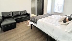 Une chambre à coucher comprenant un lit, un canapé en cuir noir, un ventilateur de plafond et une porte donnant sur une autre pièce.