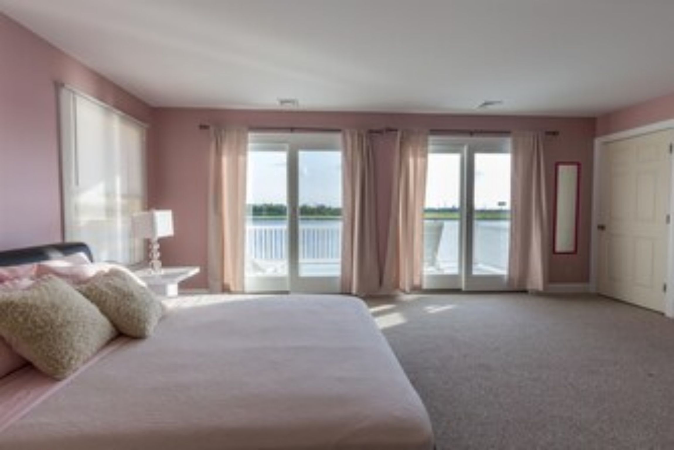 A bedroom with a large bed, a nightstand, a lamp, and a view of a balcony.
