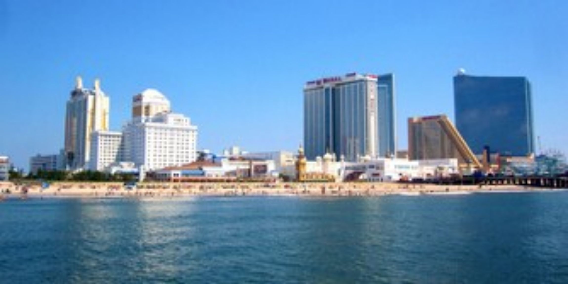 A coastal cityscape with modern high-rise buildings, a beach, and a clear blue sky.