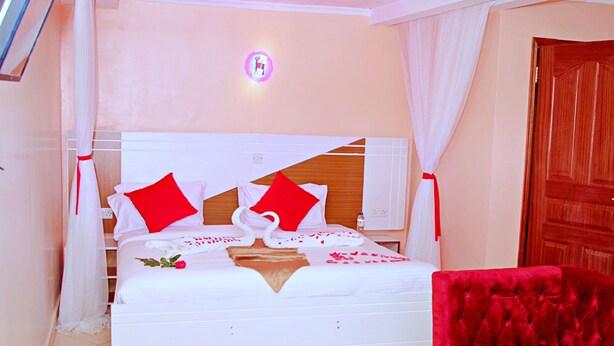 A hotel room with a bed, a red chair, and a bedside table with a bouquet of flowers. - Montana Guest Resort Naivasha  (Naivasha)
