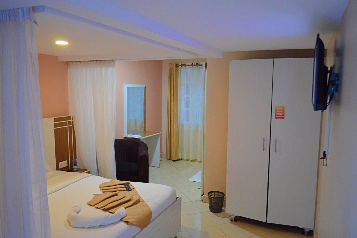 A hotel room with a bed, a desk, a wardrobe, and a television.