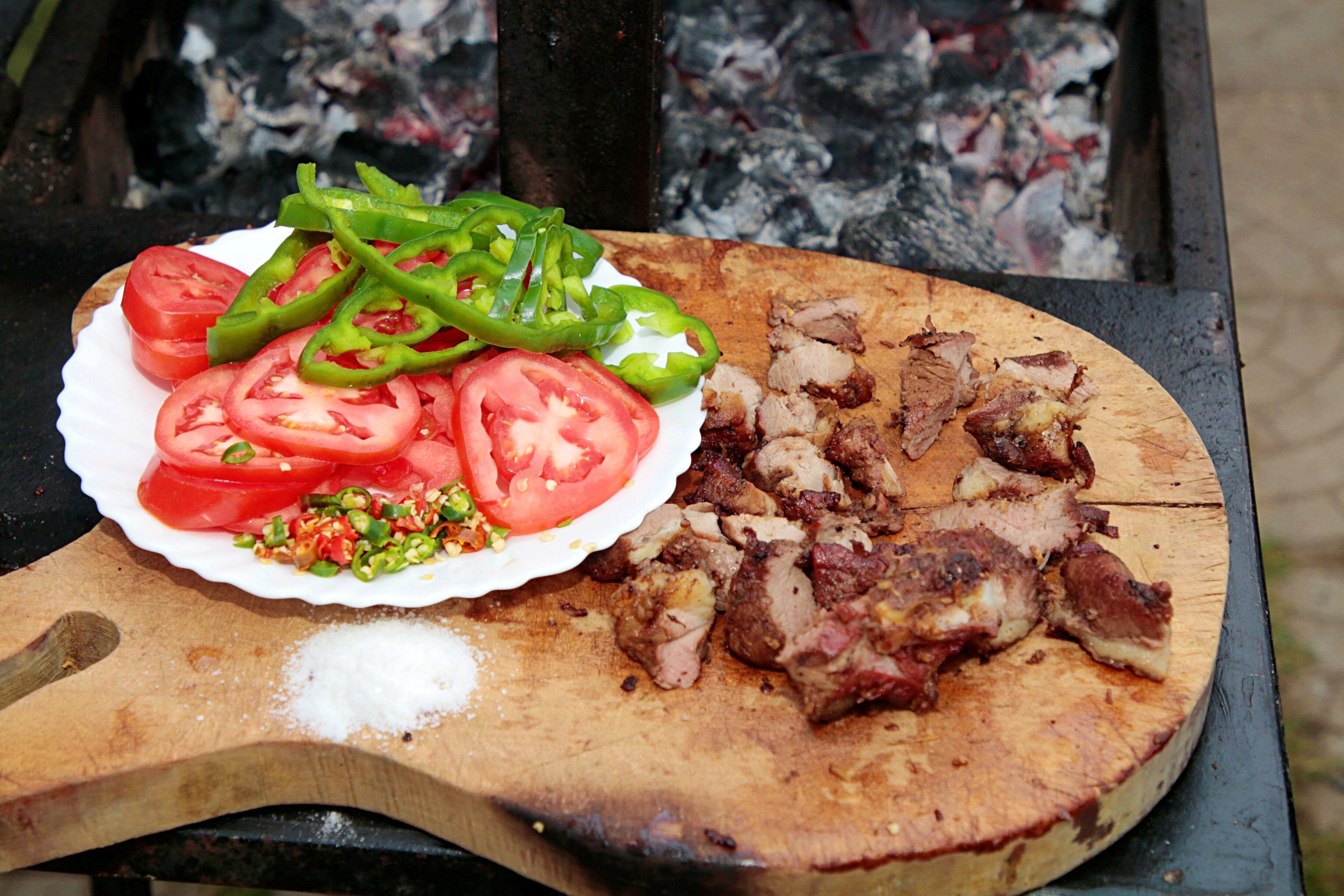 Tagliere di legno con carne affettata e un piatto di pomodori e peperoni a fette.