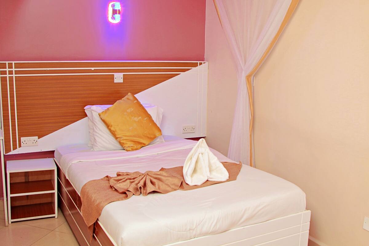A neatly made bed with white and brown bedding, a bedside table, and a wall-mounted light fixture.