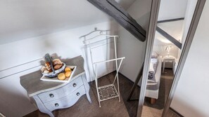 Una habitación pequeña y funcional con kitchenette que incluye una encimera blanca, un tendedero metálico y una mesita con lámpara.