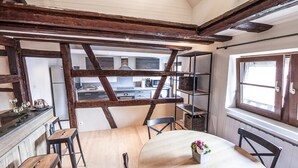 A rustic kitchen with exposed beams, a dining area with a wooden table and chairs, and a view of the kitchen through a wooden frame. - Gite 'WATCHER (Turckheim)