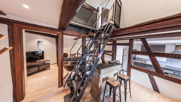 A modern interior with exposed wooden beams, a staircase, a kitchen area, and a living space with a television. - Gite 'WATCHER (Turckheim)