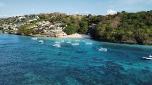 Una zona costera con barcos en aguas azul cristalino, una playa y casas en una colina.