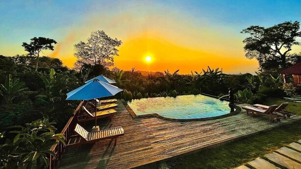 Una terraza de madera con piscina, sillas de descanso y una sombrilla azul.