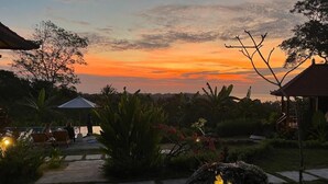 Un jardín con un sendero, un pabellón y un atardecer de fondo.