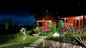 Una casa de madera con porche, sendero de piedra y plantas tropicales.