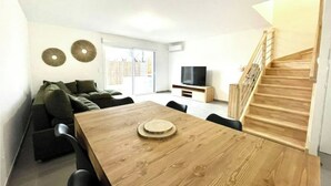 Ein modernes Wohnzimmer mit einem Holzes Esstisch, einer Couch und einem Fernseher auf einem Schrank.