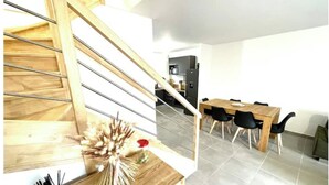 Eine moderne Küche mit einer Holztreppe, einem Essbereich mit Holztisch und -stühlen sowie einer Kücheninsel mit einer Vase getrockneter Blumen.