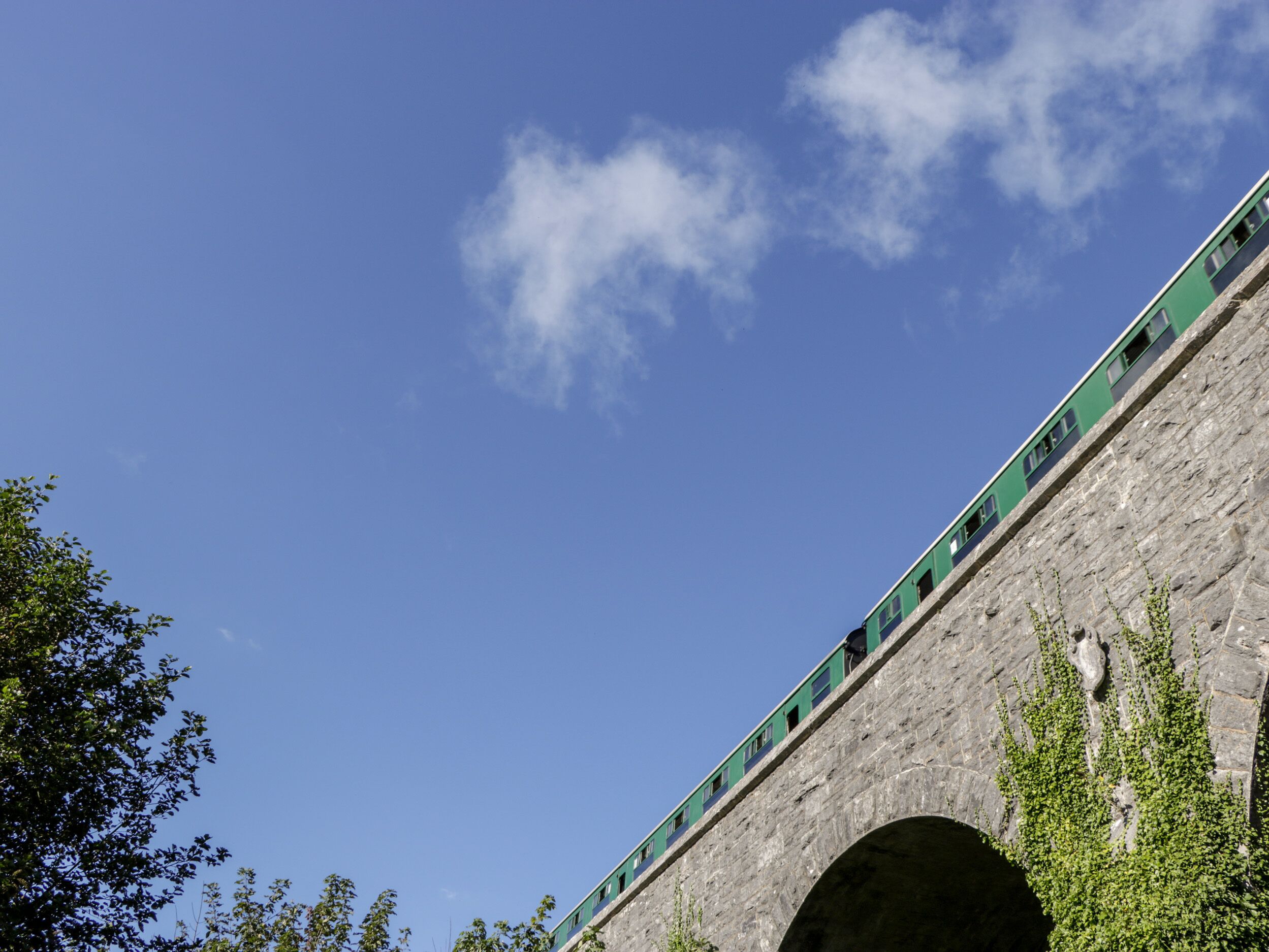 Un train vert sur un pont de pierre, avec un ciel bleu dégagé.