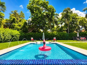 A swimming pool with a pink inflatable float, surrounded by lush greenery and a clear blue sky. - Brickell Miami Luxury Villa - 5 Suites with Private Bathrooms - Pool & Hot Tub (Miami)