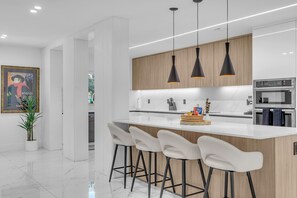 A modern kitchen with a white island, black pendant lights, and wooden cabinets.
