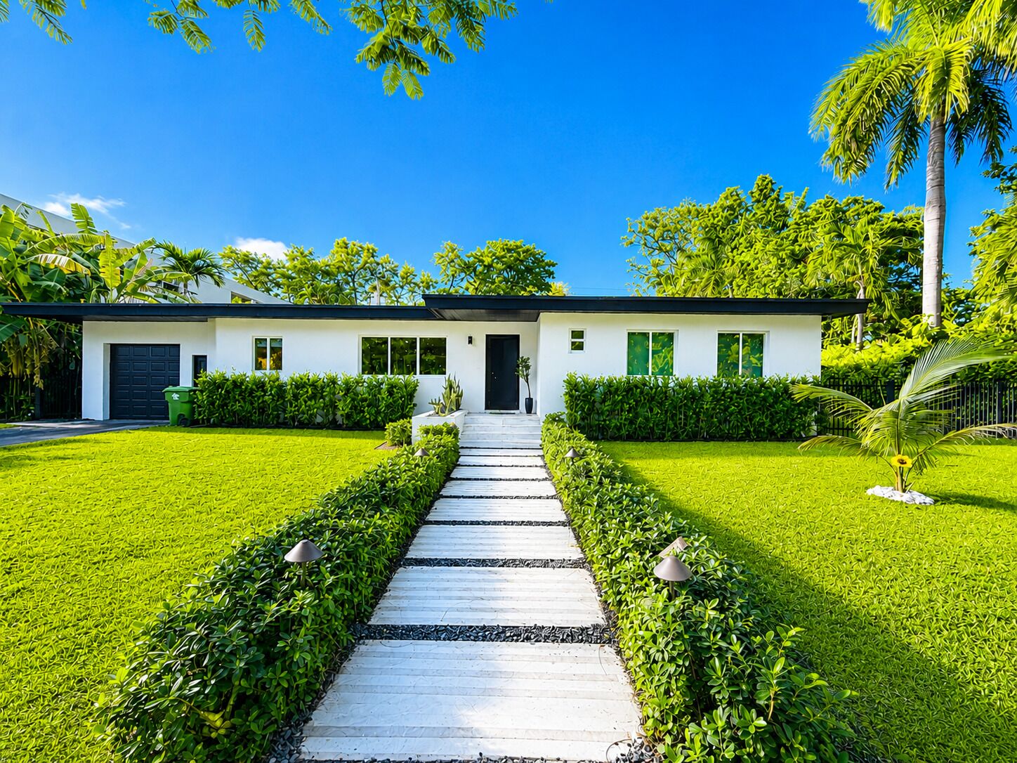 A modern two-story house with a symmetrical design, a central pathway leading to the entrance, and lush greenery surrounding the property.