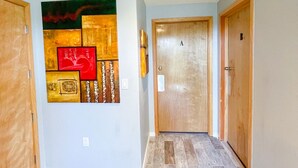 Un couloir avec des portes en bois, un ventilateur de plafond et un mur orné d’œuvres d’art abstraites.