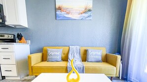 Un salon moderne avec une table blanche, un canapé jaune et un tableau représentant une scène de plage.