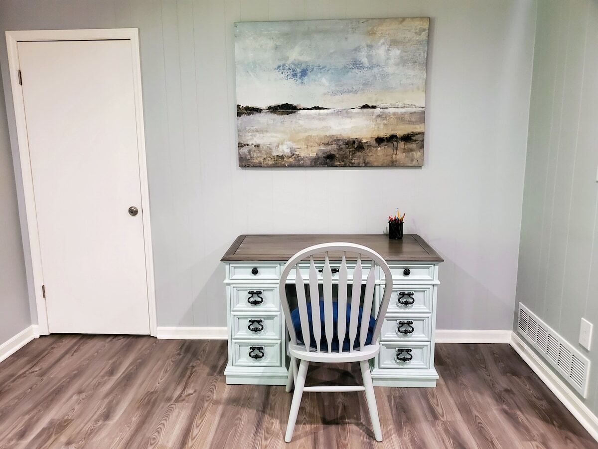 A room with a desk, chair, and a painting on the wall.