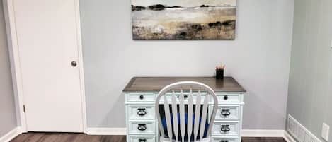 A room with a desk, chair, and a painting on the wall.