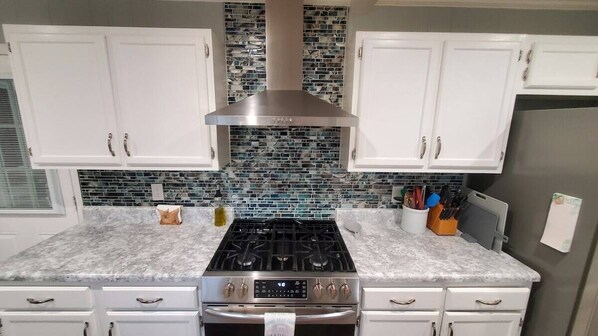 A kitchen with white cabinets, a stainless steel range hood, a tiled backsplash, and a gas stove.