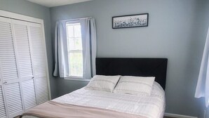 A bedroom with a bed, a window with curtains, a wall-mounted picture, and a ceiling light fixture. - Freshly Renovated Douglasville Home (Douglasville)