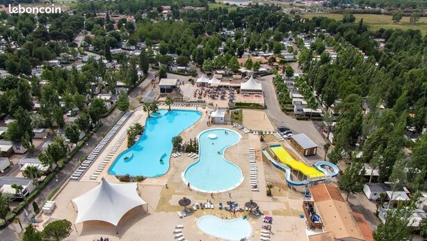 Vue aérienne d’un complexe hôtelier doté de nombreuses piscines, dont une grande piscine centrale et une plus petite piscine à la forme originale. On y trouve des espaces de détente avec des chaises longues et des parasols, ainsi qu’un toboggan aquatique.