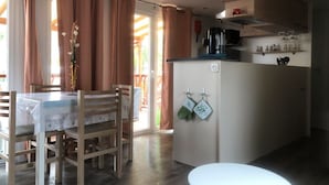 Une cuisine compacte avec un coin repas, comprenant un îlot central, des chaises en bois et une table recouverte d’une nappe en dentelle.
