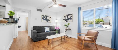 A modern living room with hardwood flooring, a gray sofa, a wooden coffee table, a brown leather armchair, and abstract art on the walls.