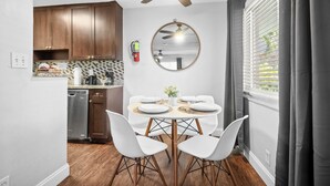 A compact kitchen with wooden cabinets, a dishwasher, and a dining area with a round table and white chairs. - The Victor Apartments by Lowk (Oakland Park)