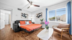 A modern bedroom with a bed, a desk, a chair, a ceiling fan, and artwork on the walls. - The Victor Apartments by Lowk (Oakland Park)