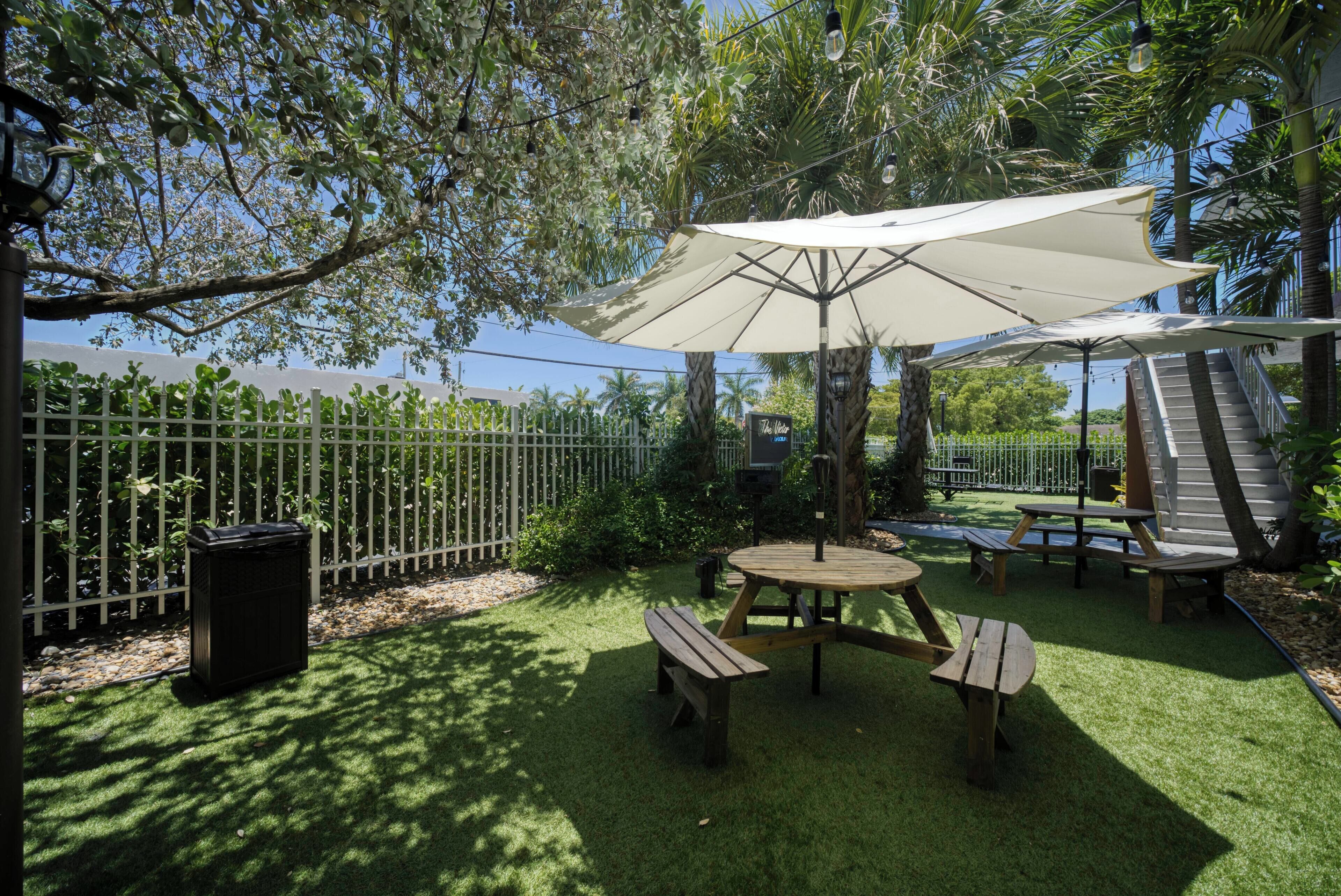 A patio area with a table and benches, surrounded by a white fence and trees.