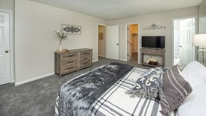 A bedroom with a bed, dresser, TV, and a door leading to another room. - 15 mins from the beach (Virginia Beach)