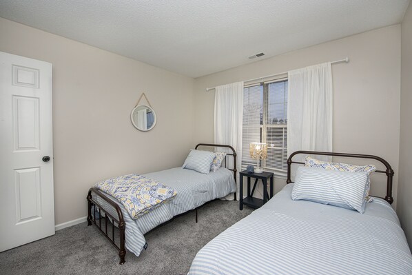 A bedroom with two single beds, a small bedside table, a mirror, and a window with curtains. - 15 mins from the beach (Virginia Beach)