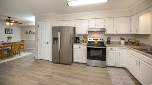 A modern kitchen with white cabinets, stainless steel appliances, and a wooden dining table. - 15 mins from the beach (Virginia Beach)