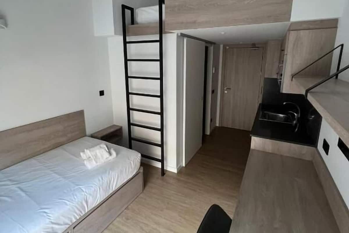 A compact bedroom with a bunk bed, a desk, and a kitchenette.