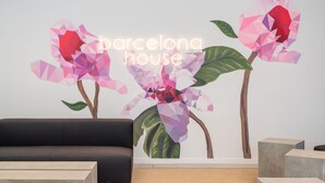 Et moderne interiør med geometrisk vægkunst af blomster, en sort sofa og minimalistisk møblering.