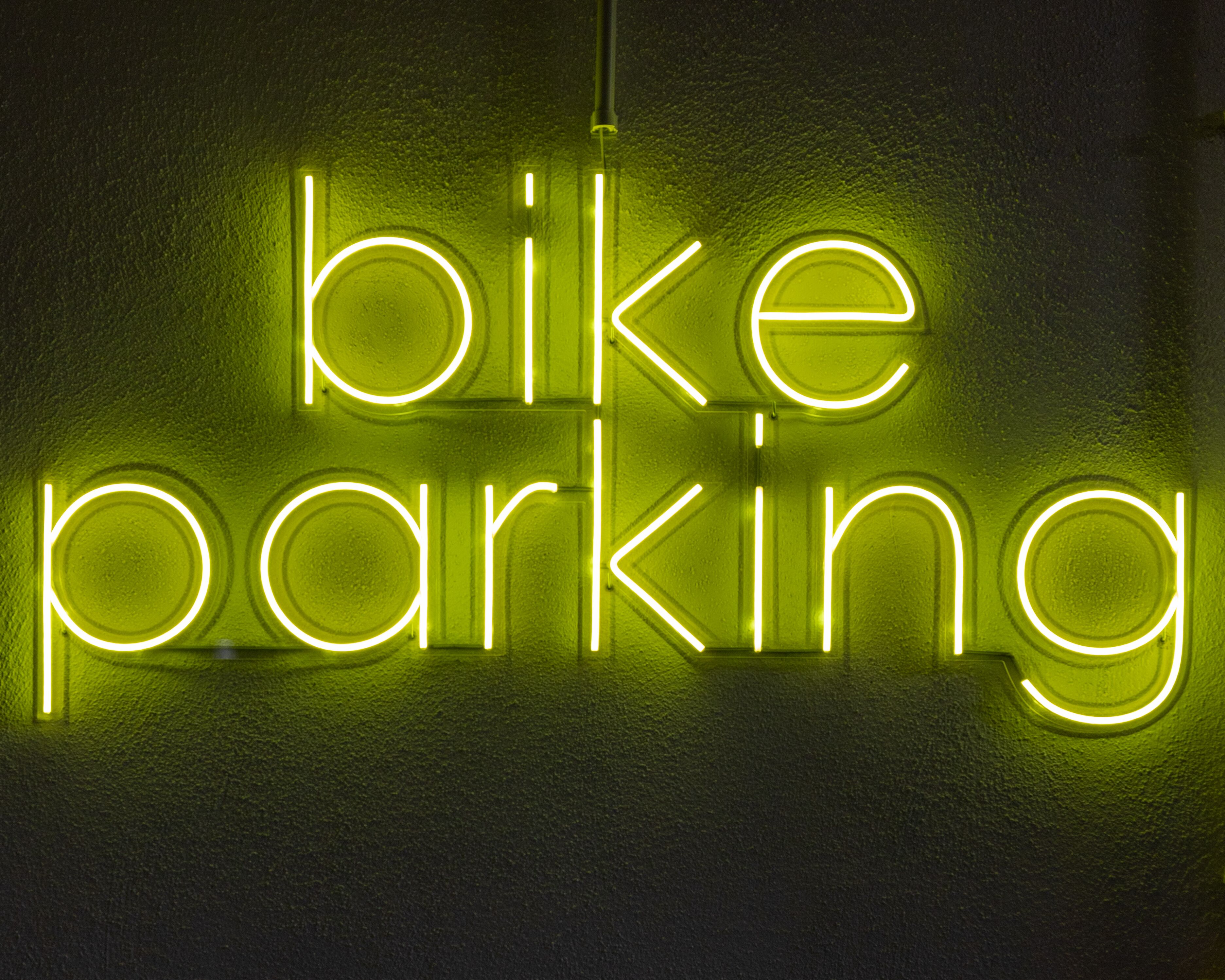 Une enseigne au néon avec les mots « stationnement vélos » sur un mur à texture.