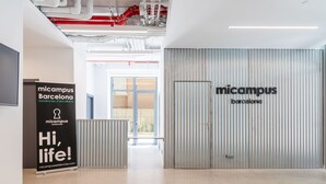 Et moderne interiør med en stor metal dør med påskriften "micampus Barcelona" og et banner med teksten "Hi, life!"