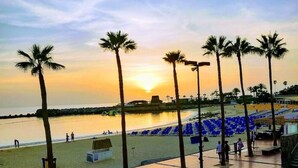 Een strand met palmbomen, een zonsondergang en een betegelde promenade.