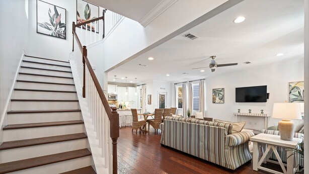 A spacious living area with a wooden staircase, a striped sofa, a dining table, and a TV on the wall.